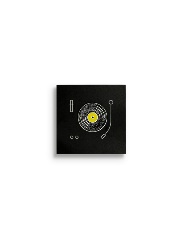 Black round metal pin with silver outline of a vinyl and yellow centre on a square black card